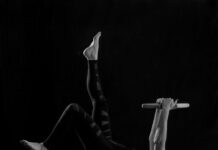 크롭티 핏의 완성, 11자 복근 : 표면이 아닌 ‘심부’를 설계하라 woman in black pants and black boots lying on black wooden bench