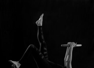 크롭티 핏의 완성, 11자 복근 : 표면이 아닌 ‘심부’를 설계하라 woman in black pants and black boots lying on black wooden bench