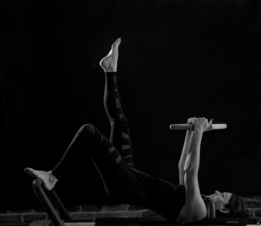 크롭티 핏의 완성, 11자 복근 : 표면이 아닌 ‘심부’를 설계하라 woman in black pants and black boots lying on black wooden bench