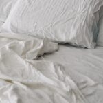 A rumpled white duvet and pillows on a bed.