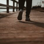 person in black pants and black shoes standing on brown wooden dock during daytime